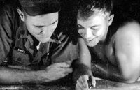 Two American soldiers huddled near each other. They appear to be looking at a map or plans.