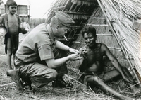 An American soldier named Hibbs helping a villager light his pipe. Hibbs has a cigarette in his mouth.