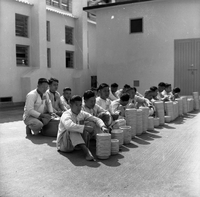 "Ai Lam - HK*" Several men sit/kneel in front of stacks of bowls.  Their uniforms suggest they may be prisoners.