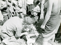 An American soldier named Hibbs examining a newborn baby. Villagers watch in the background.