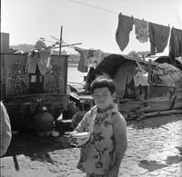 "Macau" A young boy eating rice from a bowl.  Docked boats are in the background.