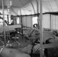 An American nurse listens to a patients breathing as she leans over his head.