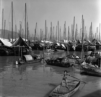 "Macau" A young boy is steering a boat in the foreground, other boats in the background.