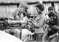 An American soldier named Hibbs is putting a band-aid on a Villager's finger. There are more villagers in the background.