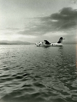 "A portion of the worlds largest airport, Cam Rahn Bay, Republic of South Vietnam, provides a parking spot for Navy SP-5B Martin Marlin from Patrol Squadron (VP) Forty. The Marlin will be replaced in mid-Apr. by the more modern P-3 Orion. VP-40 is the last operational seaplane squadron deployed to the Southeast Asia area." An American fighter jet floats on the water.  The shore and mountains can be seen in the background.