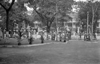 "Unidentified" Vietnamese soldiers or police stand guard inside a gated courtyard. In the street on the other side of the fence, there is a large crowd of protesters holding banners.