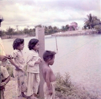 A group of children stand beside a lake.
