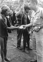 An American soldier is exchanging some sort of supply to a villager, as another American soldier named Hibbs examines another villager in the background. The supplies may be soap.