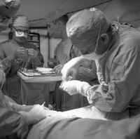 A group of American doctors are operating on a patient in a field hospital tent.