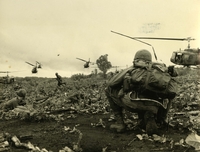 "Heliborne Airborne - Paratroopers from the 173rd Airborne Brigade, arriving by helicopter instead of by parachute, make an assault landing 28 miles southwest of Plieku during Operation 'Francis Marion'. A radioman (right) keeps on top of the situation as troopers secure the landing zone while troops carrying Huey "Slicks" move out to pick-up reinforcements." American soldiers crouch in a field, looking away from the camera as helicopters fly overhead.