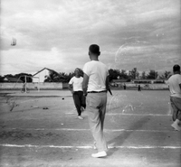 Two American men on a soccer field appear to be playing a sport - one has his back to the camera and others are seen in the background.