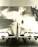 "Steam seeps through a catapult launching pad on the Seventh Fleet aircraft carrier USS Kitty Hawk, following a launching of a 43,000-pound A6 Intruder. Preparing to takeoff is another A6. These low-level attack bombers can be launched at 15-second intervals and recovered 30 seconds apart. The A6, which has among it many sophisticated instruments, radar, a computer, a television screen and inertial-navigation gear. These instruments enable the twin-jet bomber to find its way to a target and back in weather so bad that the pilot cannot see beyond his wingtip." A jet prepares to take off from an aircraft carrier.  A sailor stands in a cloud of smoke on deck, probably from another jet that just took off.