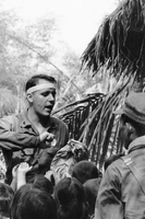 A soldier identified as Hospital Man 2nd Class Dennis Quinlan from Cincinnati is seen holding a brown paper bag as children gather around and reach for it.