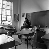 "Macau" Two nuns stand behind a desk in a classroom, looking at some papers.