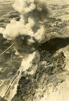 "Smoke 3,000 feet high - follows eruption of 500-foot-diameter fireball, Sep. 18, 1966, from secondary explosion at Ninh Binh railway in North Vietnam. Navy pilots from the carrier USS Intrepid continued a four-day attack on the area which included Nihnh Binh railroad yards, RR Bridge, RR by-pass bridge, two trains totaling nearly 100 boxcars, and about 60 trucks. One train is seen at lower left along a rocky ridge. Trucks along roads were trying to salvage cargo from the bottled up trains." Aerial photo of a bomb cloud over a railway.