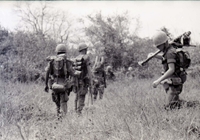 Several American soldiers walking through a field in a line.
