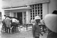 "Students wrecking min. of info." A crowd of people filing into a building. To the right of the door, five children park their bikes near a table. A man walks in front of them.