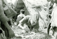 An American soldier named Hibbs examining a newborn baby. Villagers watch in the background.