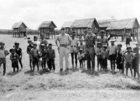 Two American soldiers, one named Hibbs, are standing in a line with many Vietnamese village children looking at the camera. There are raised village houses in the background.