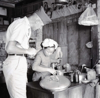 An American soldier watches a Vietnamese woman cook in a restaurant.