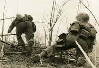 Two American Soldiers have their backs to the camera, they appear to be leaving what appears to be a trench.