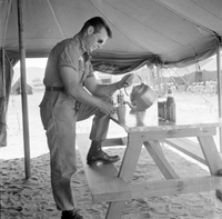 "QN + Train ", picture of a soldier getting tea from a tea pot, placed on a table, in a tent