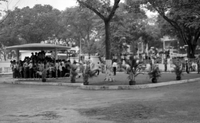 "Unidentified" A large group of people stand in a gazebo. In the background, Vietnamese soldiers or police stand guard inside a gated courtyard. In the street on the other side of the fence, there is a large crowd of protesters holding banners.