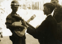 "PFC Rick Ansbro of Levittown, Pennsylvania, accompanies Brother Paul Trung in an arrangement of 'The Yellow Submarine.' Brother Trung, one of Vietnamese Catholic priests in charge of the Christian Brothers School, in an accomplished guitarist and speaks English fluently." An American soldier and a Vietnamese Catholic priest play guitar and sing together.