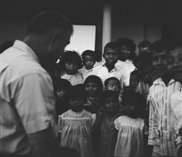 "Ca Mau" Crowd of young Vietnamese children around a man.