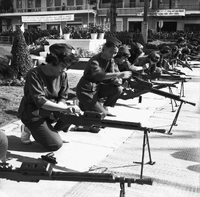 Original caption: "Mne. Nhu + Paramilit. Graduation - 27 Feb 63" Several Vietnamese women are loading guns in a line. (different angle)