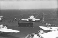 Naval planes on an aircraft carrier in open water. A group of American men are working on something on the runway.