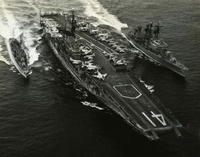 USS Midway, an American aircraft carrier, on the sea. There are two smaller naval ships beside it.