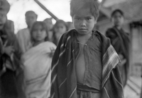 "BMT" [BuÃ´n Ma Thuá»™t], a young Vietnamese boy wrapped in a blanket stares intensely at the camera. More children stand out of focus in the background.