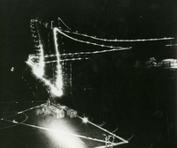 "As the American servicemen look around in Vietnam he sees many scenes to remind him of the fourth of the July fireworks displays he so vividly remembers at home. What he sees though is not fireworks celebrating independence for South Vietnam. This night, time exposure was taken from the fast combat support ship USS Sacramento. The lights are the running lights on a vertical replenishment helicopter used for the replenishment of U.S. Seventh Fleet ships." A long exposure photograph of a light moving above a helicopter landing pad.