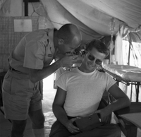 An American doctor looks into a soldiers ear as the patient smiles.