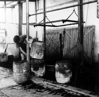 "Indonesian Arts and Crafts Negs [Negatives]." An Indonesian man stacks dyeing barrels in a large warehouse-style room. From a scrapbook page 10.