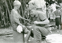 An American soldier named "Hibbs" giving medical treatment and inspecting an injured villager's hand.