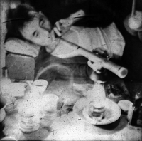 Photo from Beverly Keever's visit to a Singapore opium den. A man reclines on the floor with a pipe in his hands. A lamp, a cup, and some bottles sit in front of him.