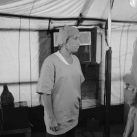 A nurse stands in surgery scrubs as she looks away from the camera.