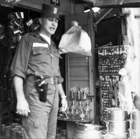 "Ca Mau" American soldier stands in front of what appears to be a market or store front. (blurry)