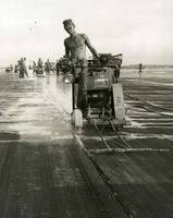"A diamond saw bites into Chu Lai's two-mile Main Runway as Seabees from MCB 71 hurry to complete repairs on the damaged center seam. Lester Carroll, 19, from San Antonio, Texas, a member of Seventy-One's Charley Company guides his gas-powered saw along the seam. A constant supply of water was used to lubricate the work. As many as ten of the power saws were at work at one time on a 2-mile runway. The Seabees finished the project 4 days ahead of schedule...'in keeping with the tradition of the Seabees,' said Commodore Turner of third Naval Construction Brigade." American soldiers cut a narrow ditch in an air field runway with a large saw.