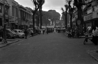"Unidentified", Photo of a protest. A large crowd of Vietnamese people walk in a tree lined street with banners. The street is lined with small shops, and pedestrians have paused to watch.