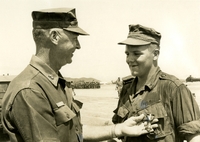"Leadership in Action - Cpl. Bryant C. Collins (right) (Hartford, Conn.) talks to MajGen. Wood B. Kyle, 3rd Marine Division commanding general, after he was awarded the Navy Cross during Memorial Day ceremonies at Phu Bai. Collins received the United States' second highest combat award for personally killing 11 Viet Cong during a four-hour battle and taking command of hs reconnaissance patrol and leading them safely from deep in enemy territory after his company commander was killed." A US military officer pins a medal to the chest of a soldier. A military camp is in the background.