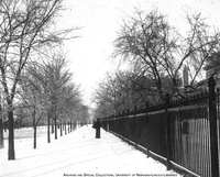 View lookng north of iron fence along R street around 1900. University Hall appears in the back, left, and the Chemistry Laboratory to the right. View Image