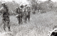 Several American soldiers walking through a field in a line.