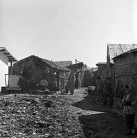"Macau" A slum street, filled with villagers, including several children.  A pile of rubble or trash is in the foreground.