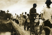 "Residents of An Xuan Hamlet promenade across their new bridge after the bridge was turned over to the people by the 18th MP Brigade and 20th Engineering Brigade, the joint sponsors." Vietnamese children, an American soldier, and villagers walk across a bridge.