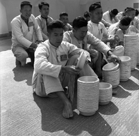 "Ai Lam - HK*" Several men sit/kneel in front of stacks of bowls.  Their uniforms suggest they may be prisoners.