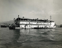"Hatch Teams 'Home' - This floating berthing vessel (APL 30) is 'home' to 30 hatch teams that work the holds of cargo vessels at anchor in Da Nang harbor. Berthing spaces aboard are air-conditioned for crewman's comfort." A large berthing ship anchored offshore.