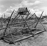 "Montagnards - Showplace Strat. Ham - 8-21-62 - In MTs - Faces - Blockhouses" A wooden structure is pictured near a fence.